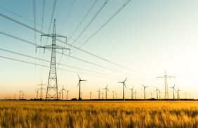 Windräder und Hochspannungsmasten, davor Getreidefelder